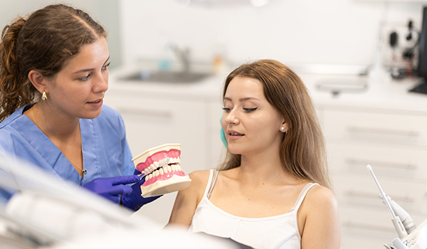 dental professional explaining oral hygiene to a patient showing an 8 tooth model in a clinic setting